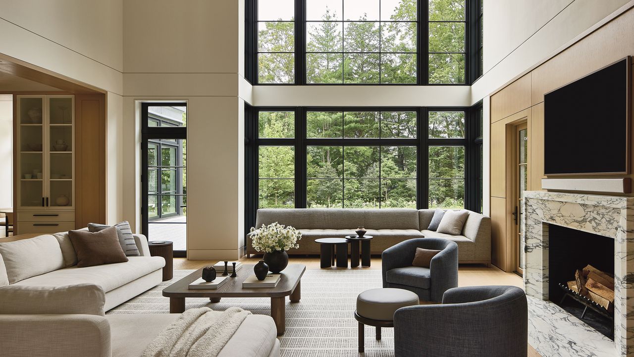 Warm modern interior with high windows, fireplace, and pale furnishings